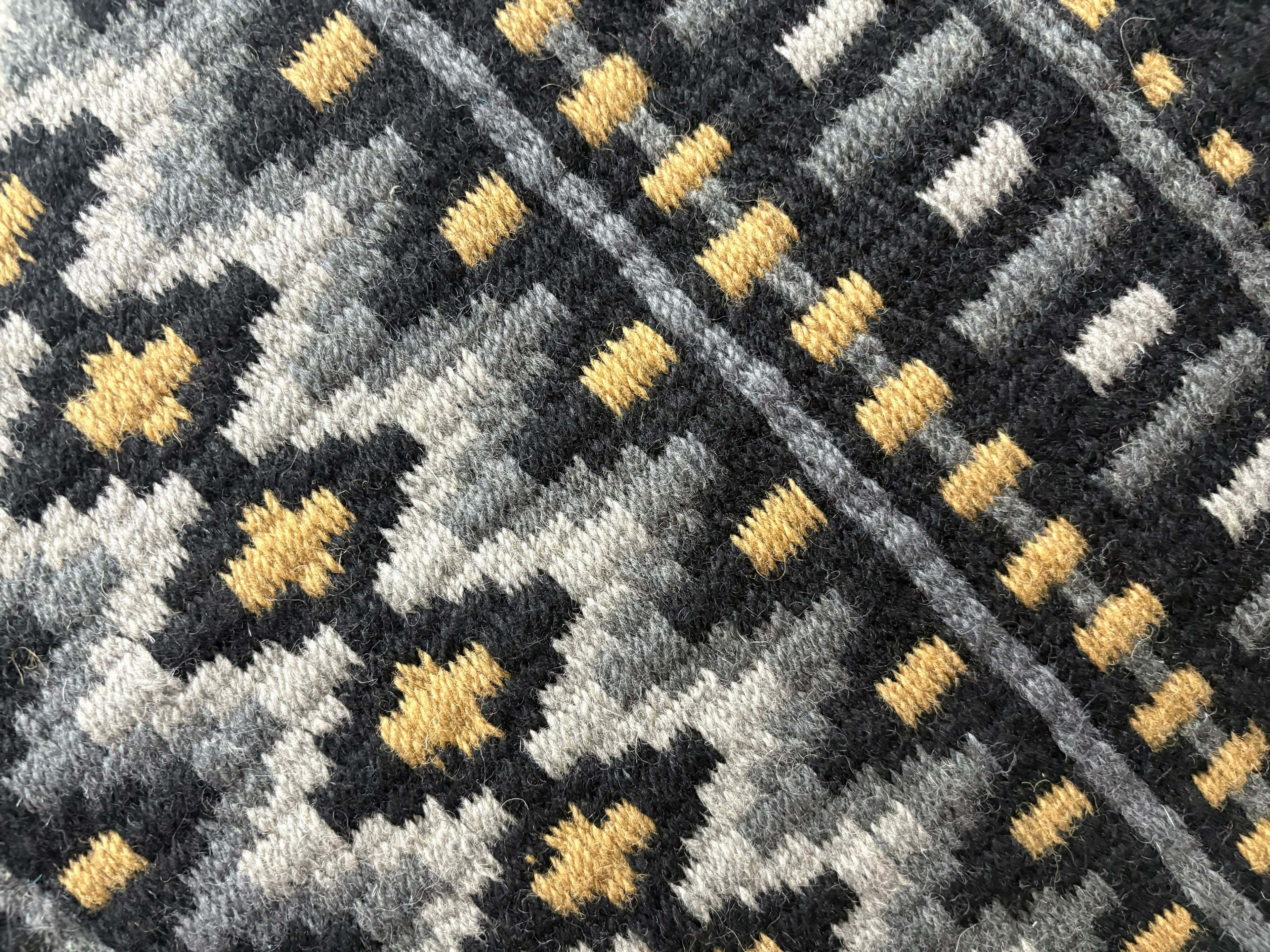 Extreme close-up detail of the hand-woven wool weave on a black, grey, and gold geometric western show pad showing texture and pattern stitching