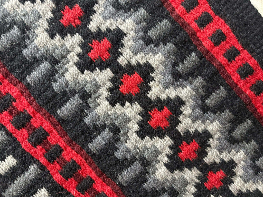 Extreme close-up detail of the tight handloom wool weave on a black, silver-grey, and red geometric western show pad.