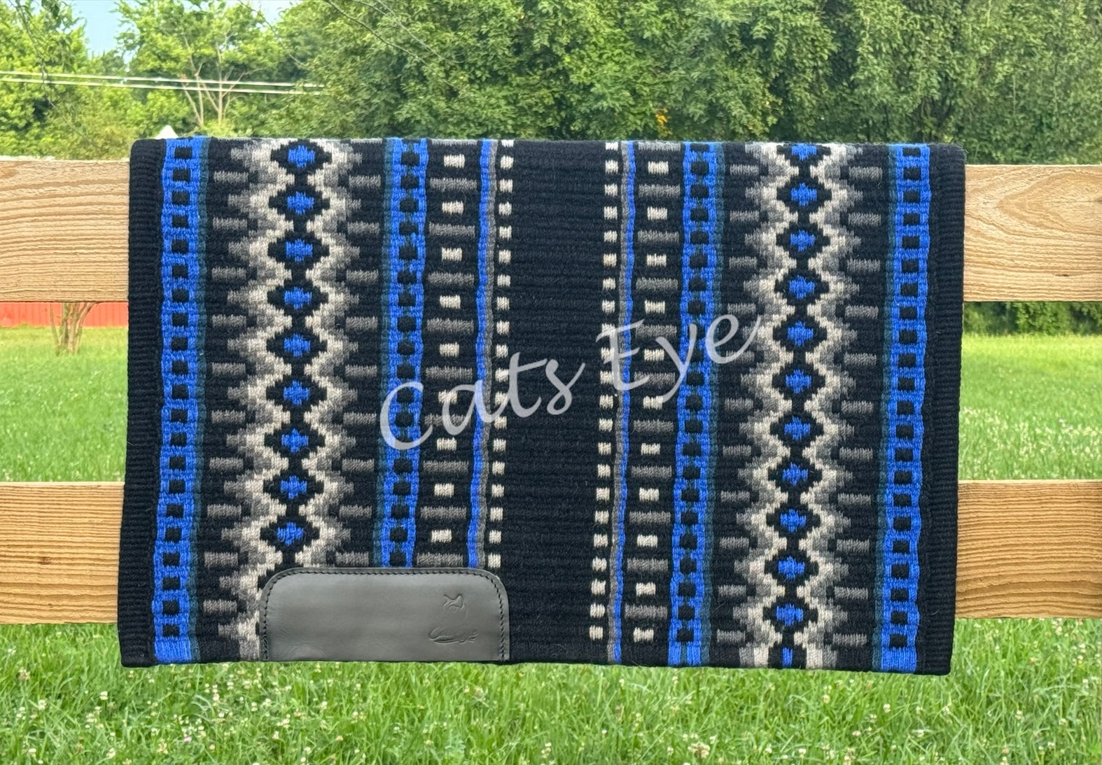 hand-woven western show pad with a black base featuring geometric diamond patterns in charcoal, silver grey, and vibrant royal blue accents with black wear leathers