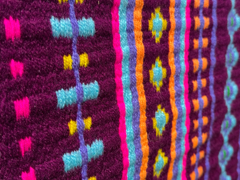 Extreme close-up detail of the tight handloom wool weave on a magenta plum-berry geometric western show pad with bright orange, light turquoise, hot pink, and yellow accents.