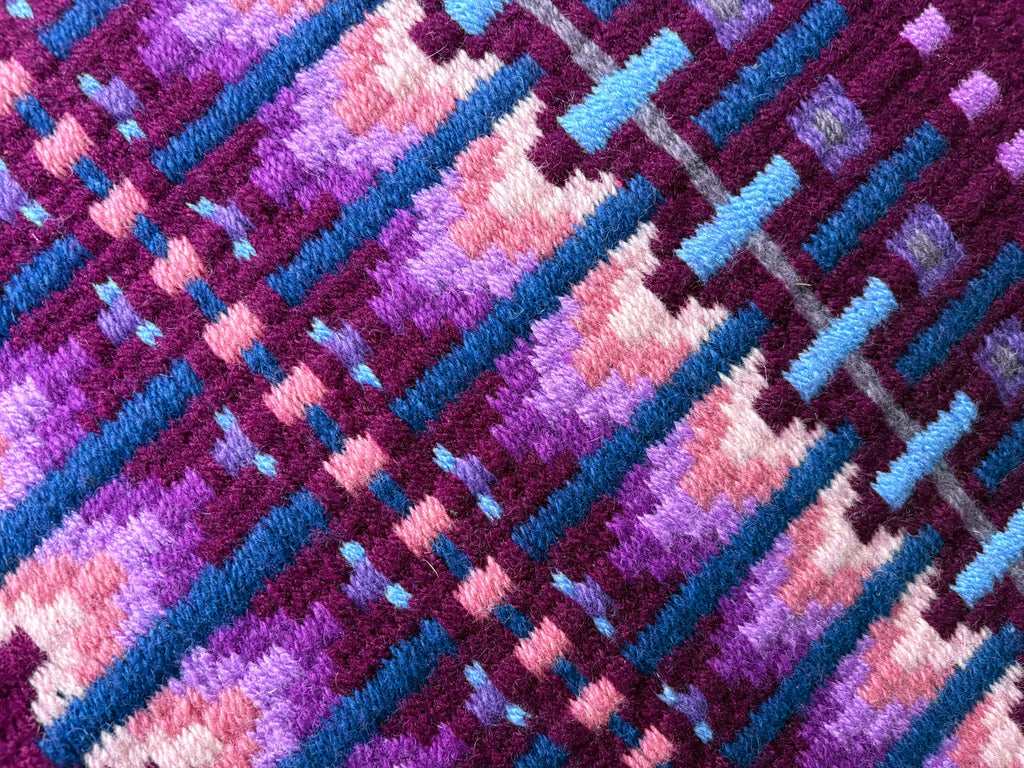 Extreme close-up detail of the tight handloom wool weave on a deep magenta berry geometric western show pad with bright purple, soft pink, periwinkle, and light blue accents.