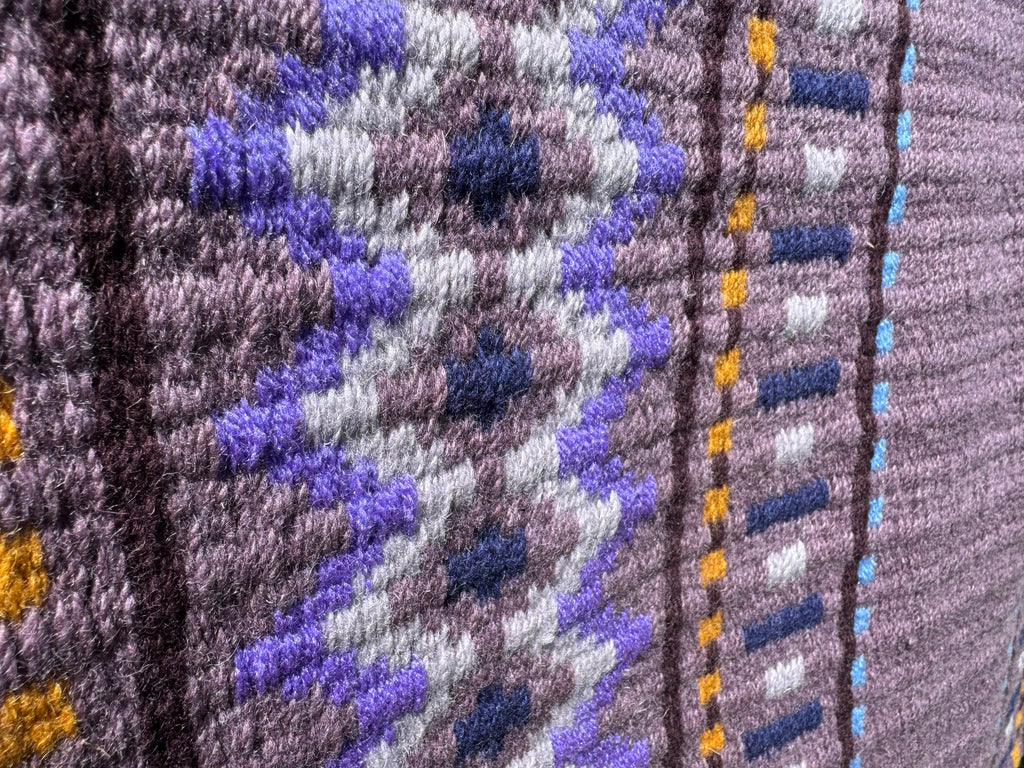 Extreme close-up detail of the tight handloom wool weave on a dusty mauve geometric western show pad with periwinkle lavender, deep purple, crisp white, light cyan, and marigold yellow accents.