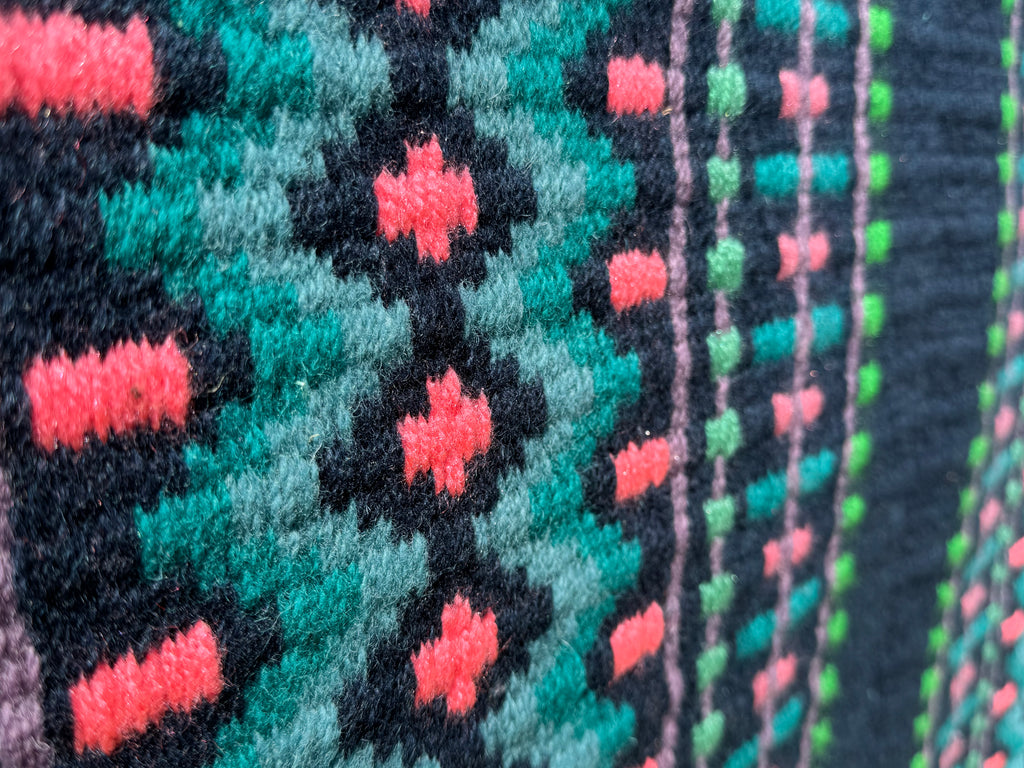 Extreme close-up detail of the tight handloom wool weave on a midnight navy blue geometric western show pad with bright turquoise, coral-pink, muted lavender purple, and lime green accents.