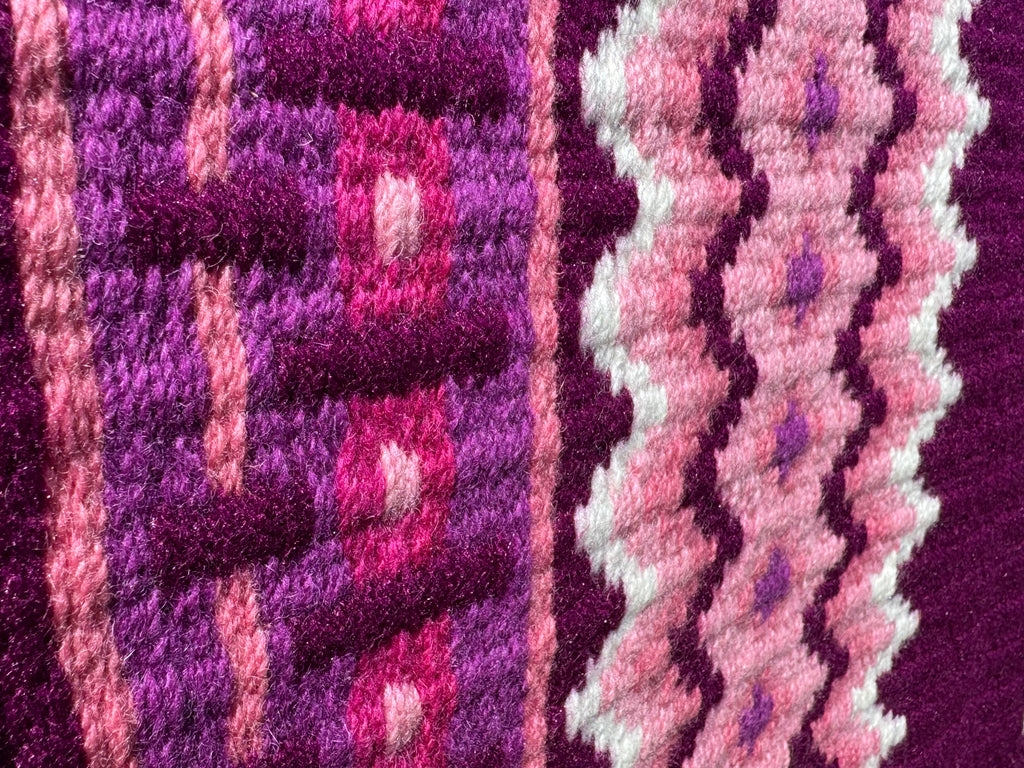 Extreme close-up detail of the tight handloom wool weave on a plum-berry geometric western show pad with light pink, crisp white, dark magenta, and hot pink accents.