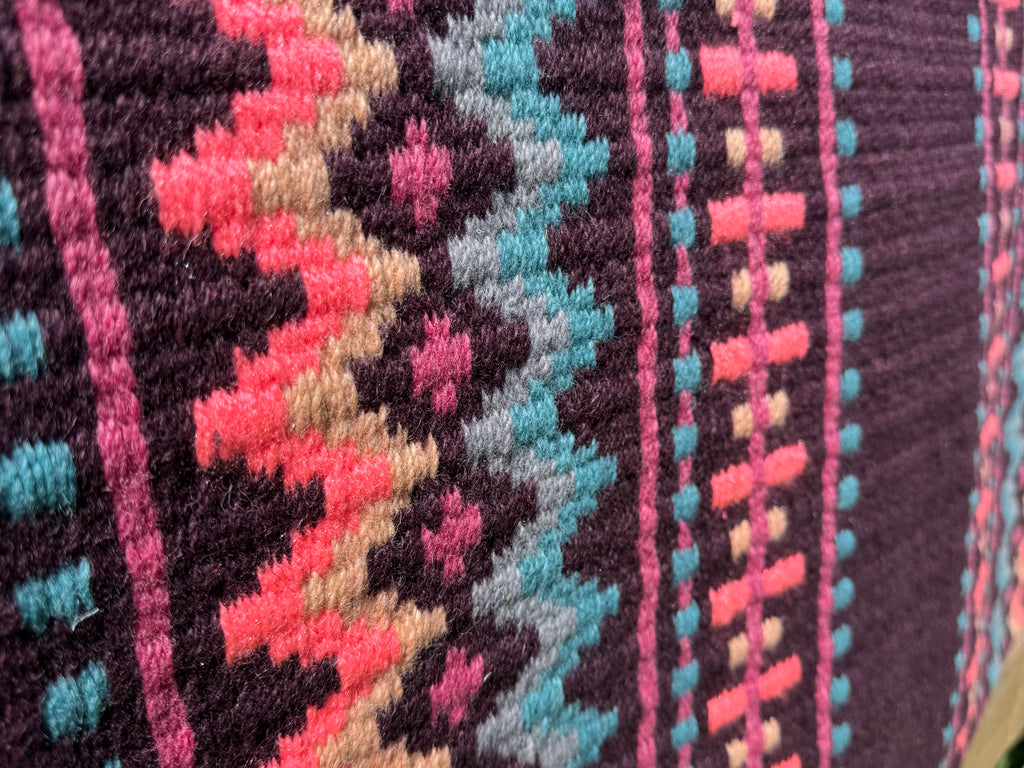 Extreme close-up detail of the tight handloom wool weave on a dark plum geometric western show pad with turquoise, sandy beige, vibrant hot pink, and magenta accents.