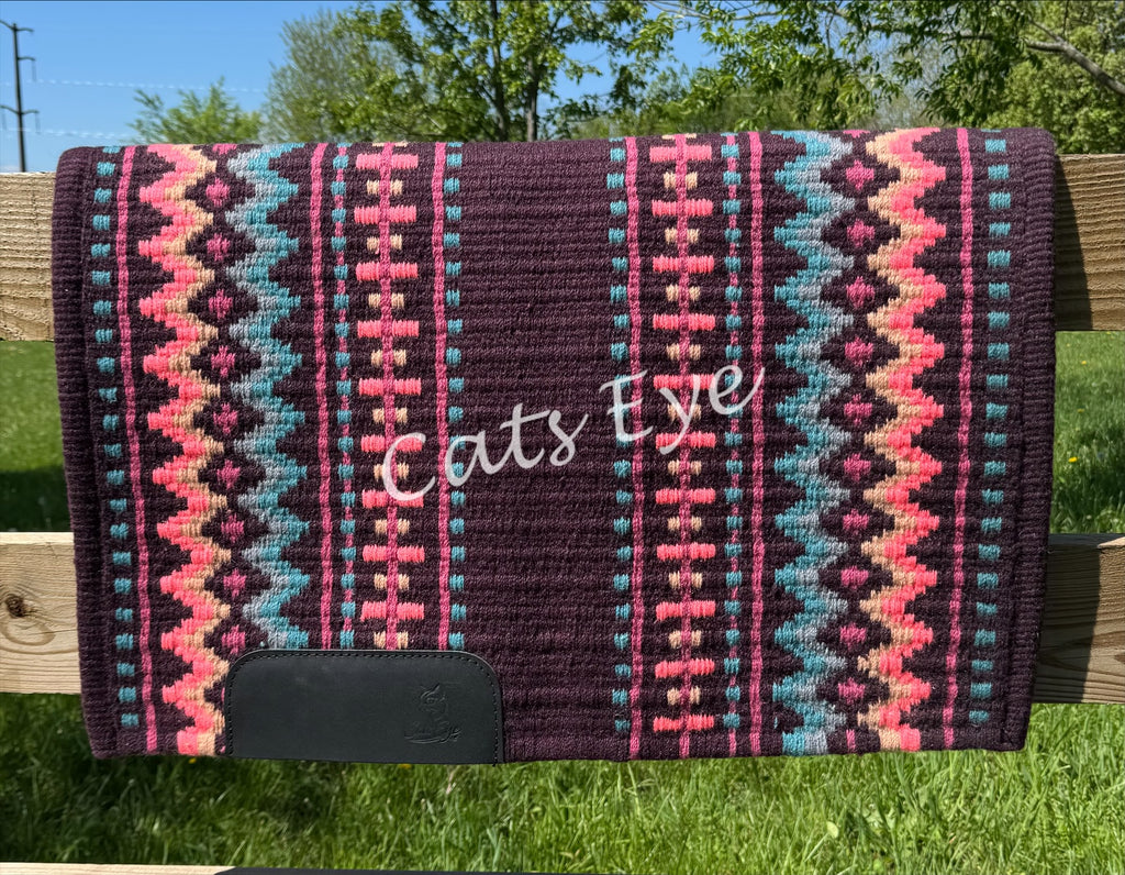 Hand-woven western show pad with a dark plum base featuring geometric diamond patterns in turquoise, sandy beige, vibrant hot pink, and peach accents with black wear leathers.