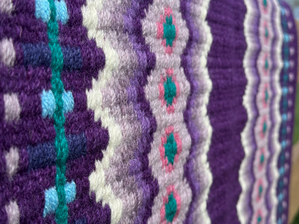 Extreme close-up detail of the tight handloom wool weave on a royal purple geometric western show pad with lavender, cream, bright pink, and teal accents. 