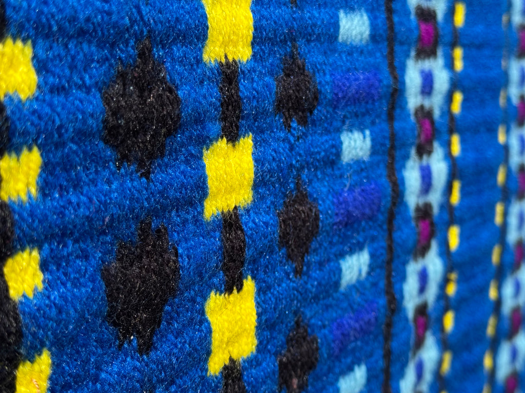 Extreme close-up detail of the tight handloom wool weave on a bright royal blue geometric western show pad with vibrant yellow, black, maroon, and light turquoise blue accents.