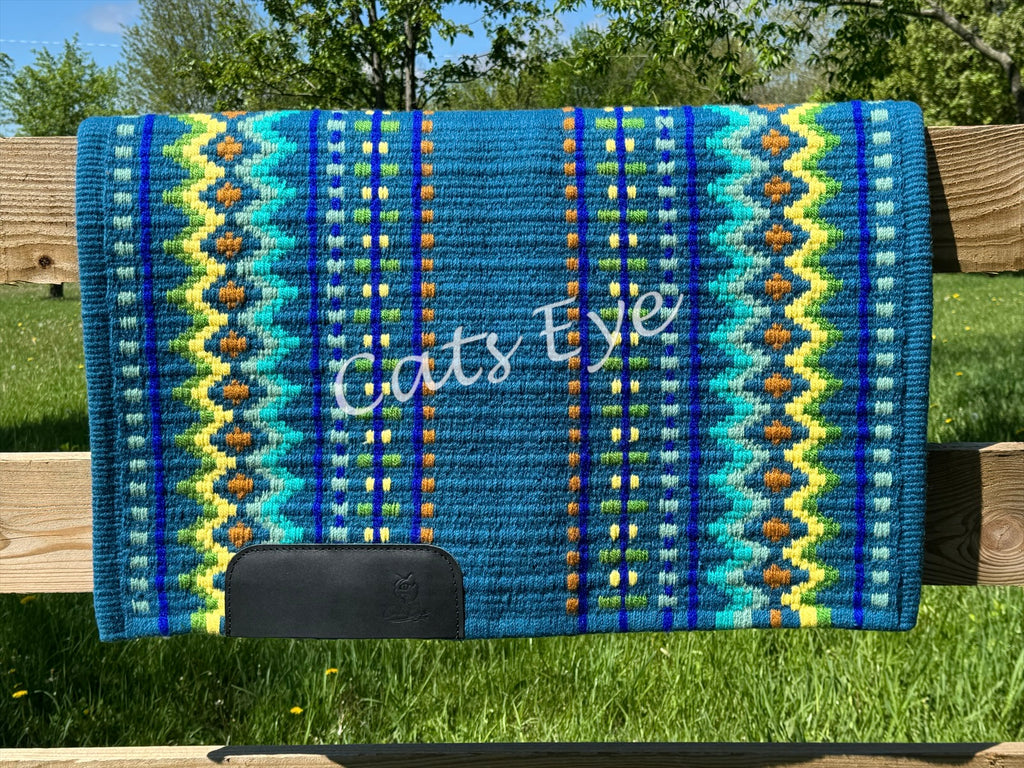 Hand-woven western show pad with a rich teal blue base featuring geometric diamond patterns in lime green, bright yellow, royal blue, turquoise, and rust orange accents with black wear leathers. 